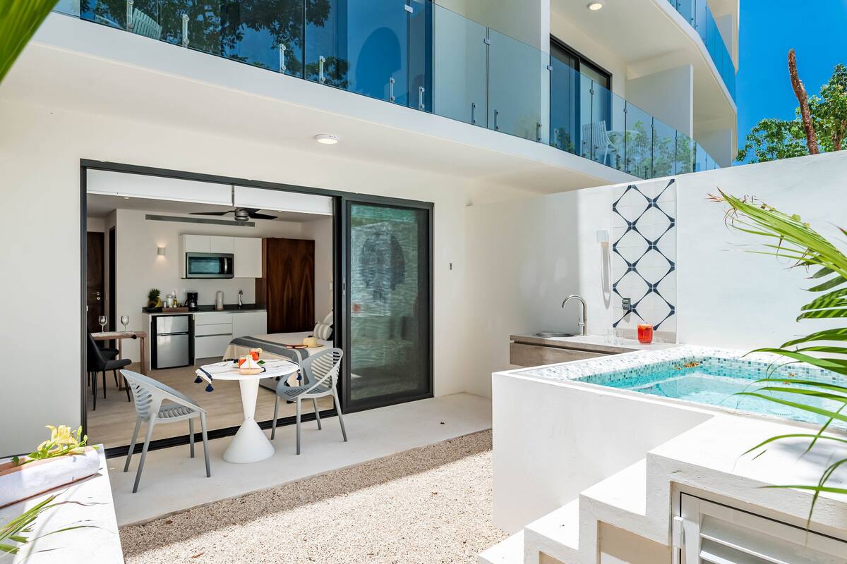 A modern outdoor living area with a dining table, chairs, a kitchen, and a pool.