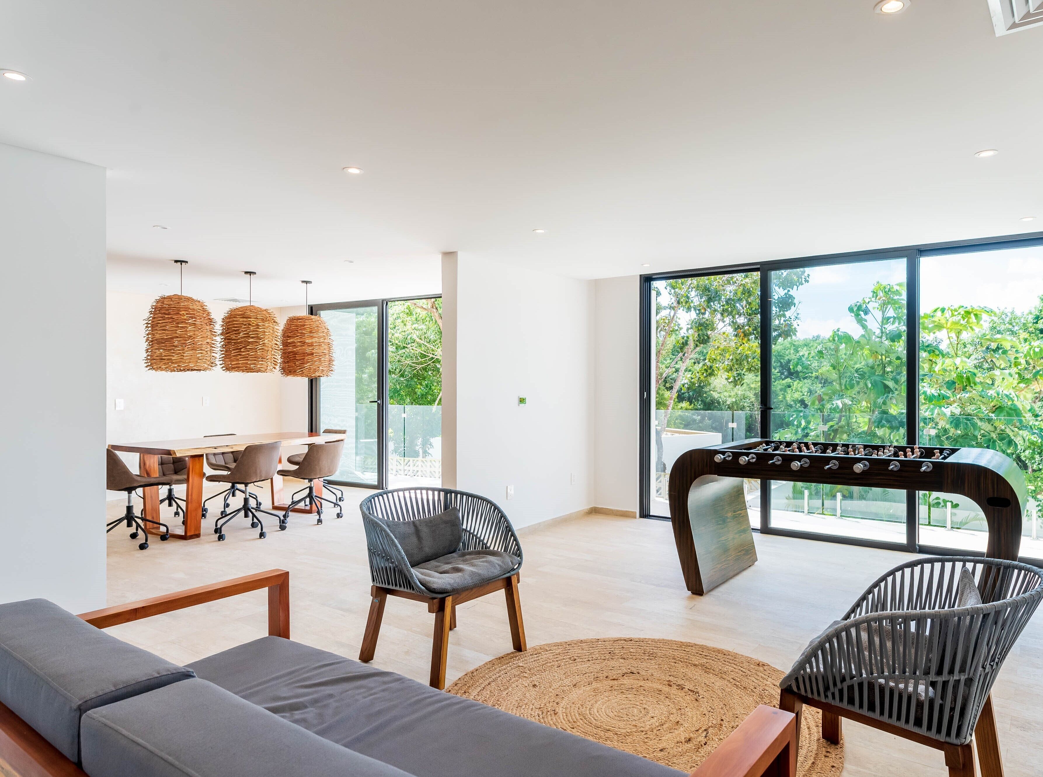 A modern living room with a sofa, chairs, a dining table, and a foosball table.