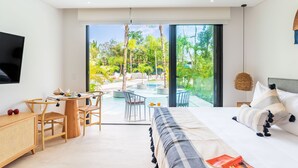 Una habitación de hotel moderna con una cama grande, un escritorio con una silla, una mesita y vistas a un área de piscina al aire libre.