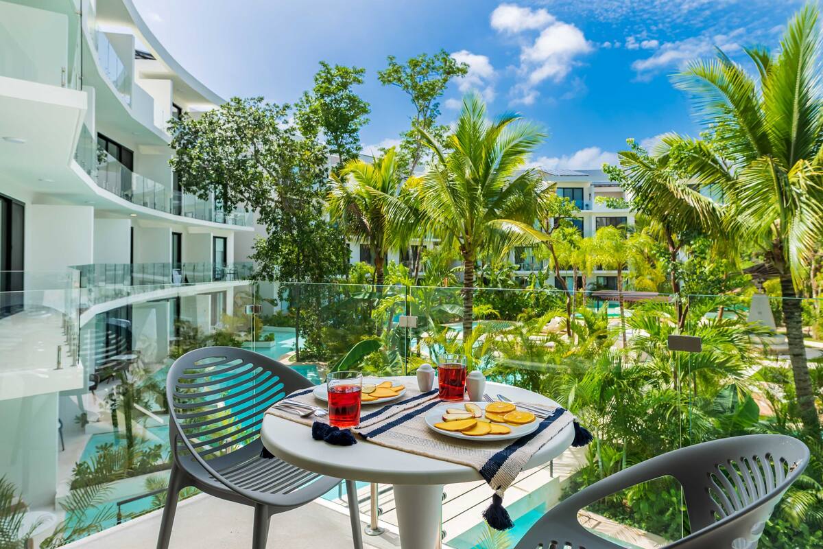A balcony with a table set for two, overlooking a pool and lush greenery.