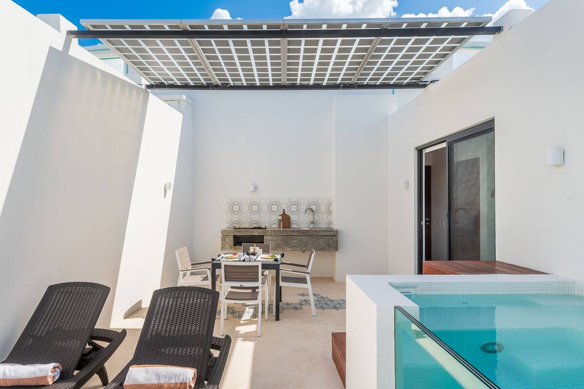 A rooftop patio with a pool, lounge chairs, a dining table, and a grill area.
