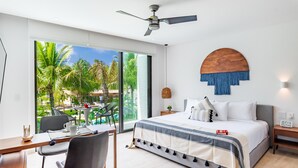 Una habitación de hotel moderna con una cama grande, un escritorio y vistas a un jardín tropical.