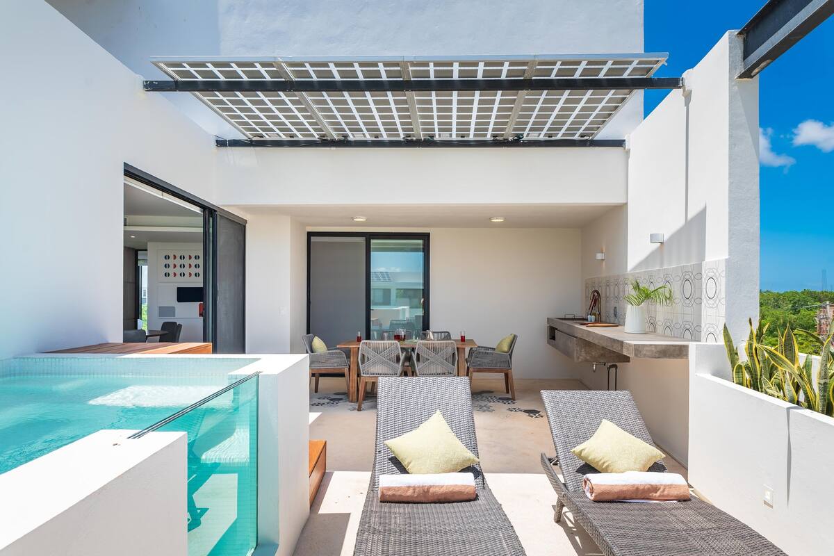 A modern outdoor space with a pool, lounge chairs, a dining area, and a kitchen.