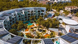 Un hotel moderno con distribución circular, paneles solares, un patio central con fuente y abundante vegetación circundante.