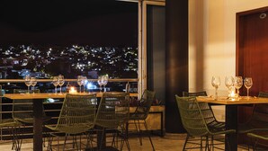 A restaurant with outdoor seating, tables with chairs, and a view of a cityscape at night.