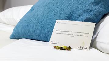 Una habitación de hotel con una cama blanca, un almohadón azul, una tarjeta con una cita y un regalo envuelto.