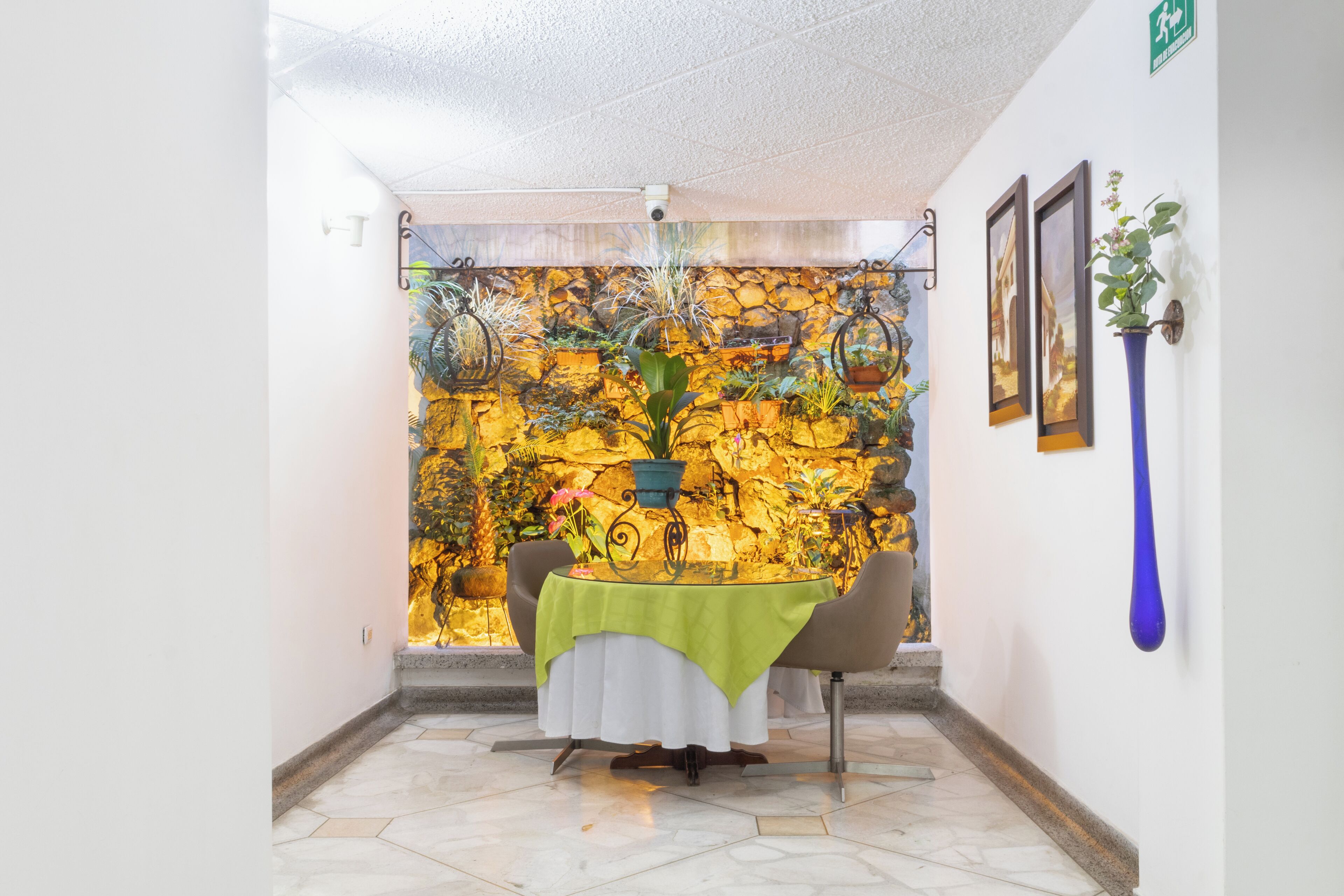 A dining area with a table set for two, a stone wall with plants, and a blue vase on the wall.