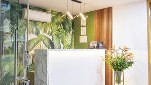 A reception desk with a green wall, a wooden slat wall, and a potted plant.