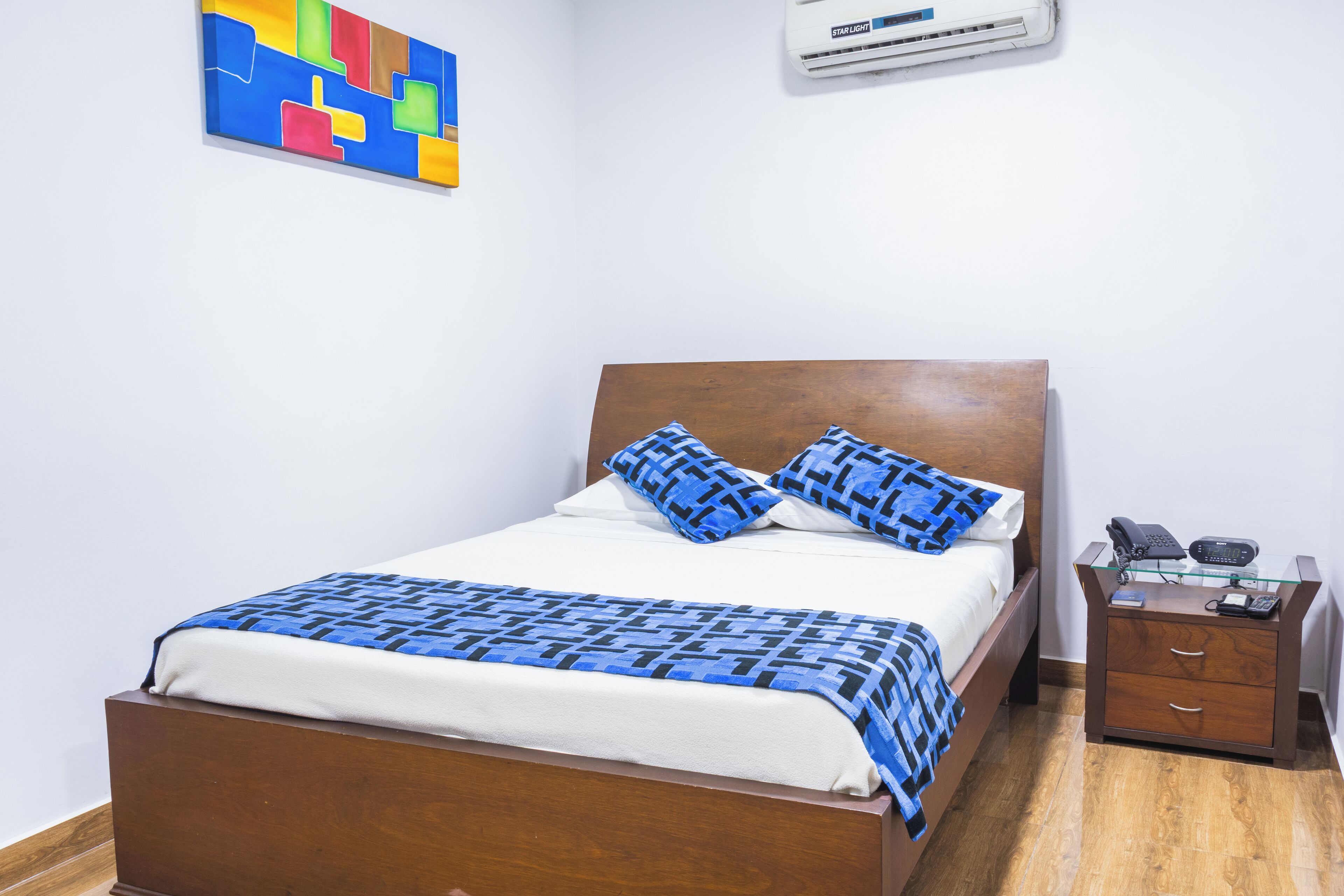 A neatly made bed with a patterned bedspread, a wooden headboard, and a bedside table with a telephone and a book.