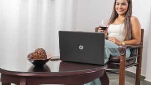 A person sitting at a table with a laptop and a glass of red wine.