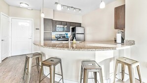 Una cocina moderna con una isla central, electrodomésticos de acero inoxidable y taburetes de bar.