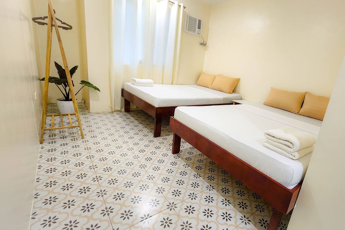 A hotel room with two single beds, a wooden ladder, a potted plant, and a tiled floor.