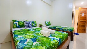 Habitación de hotel con una cama grande, ropa de cama con estampado de hojas tropicales, dos almohadas y toallas dobladas con cuidado.