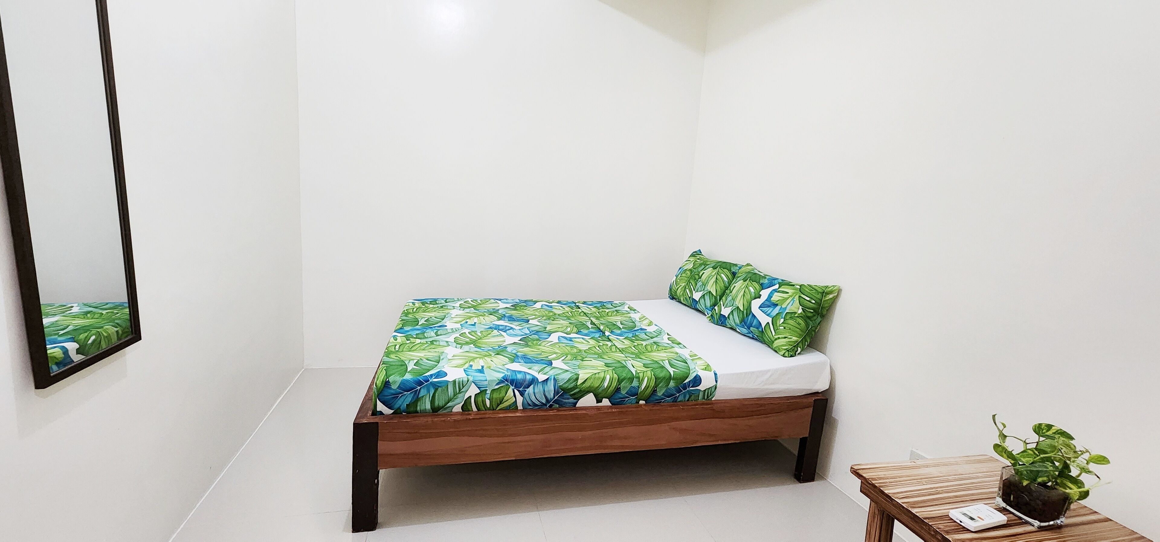Une petite chambre à coucher, bien rangée, avec un lit, une table de chevet et une plante en pot.