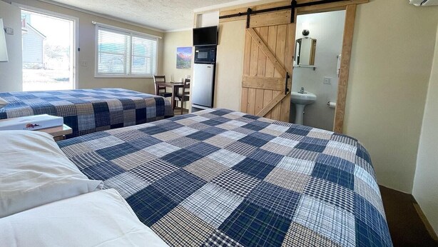 A bedroom with two beds, a dining table, a microwave, a sink, and a sliding barn door. - Mt Carmel Motel Room close to Zion National Park! (Orderville)