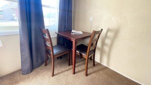 Un pequeño comedor con una mesa y cuatro sillas, una ventana con cortinas y piso alfombrado.