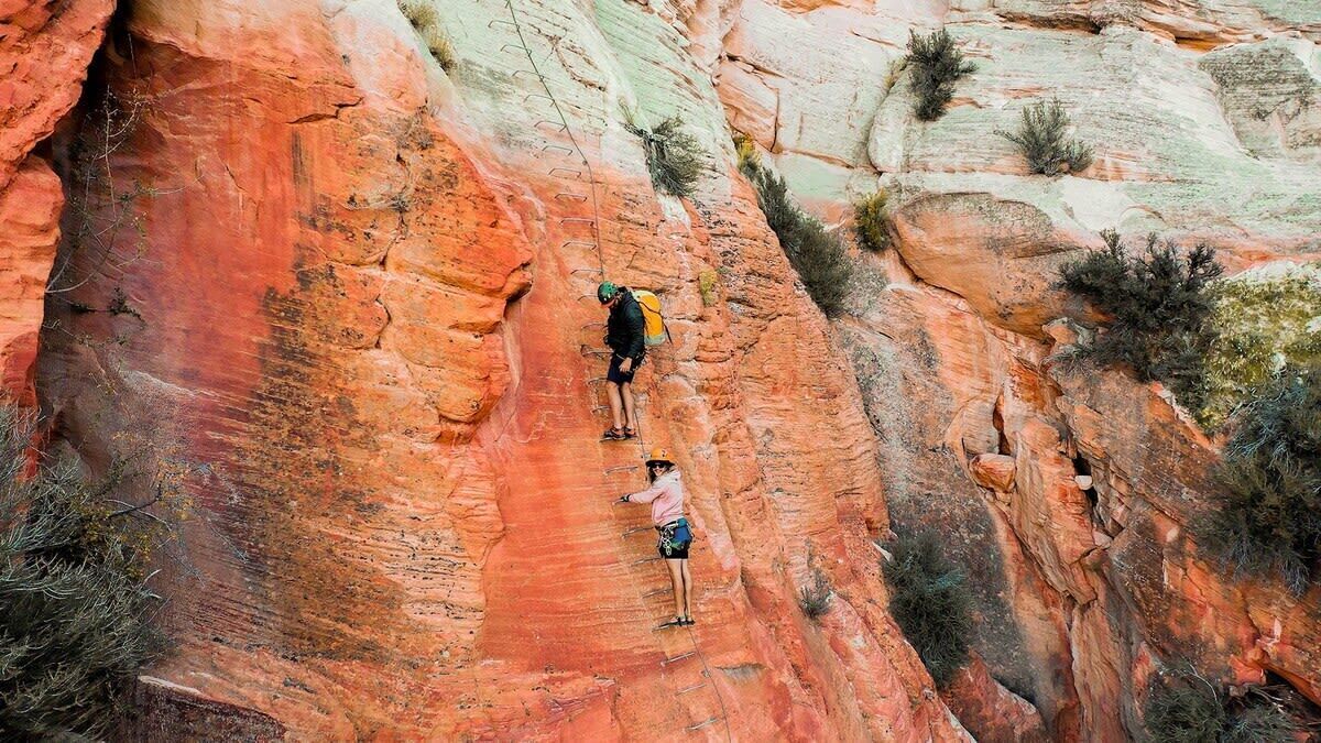 Une personne escalade une formation rocheuse rouge.