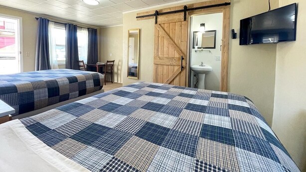 Una habitación de hotel con dos camas, un escritorio, un espejo, un televisor y una puerta corredera.