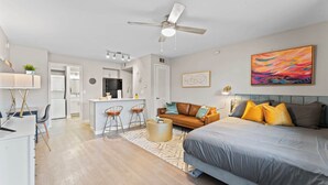 A modern apartment with a kitchen, dining area, and a bedroom with a large bed and colorful pillows. - Charming studio close to Downtown and Domain (Austin)