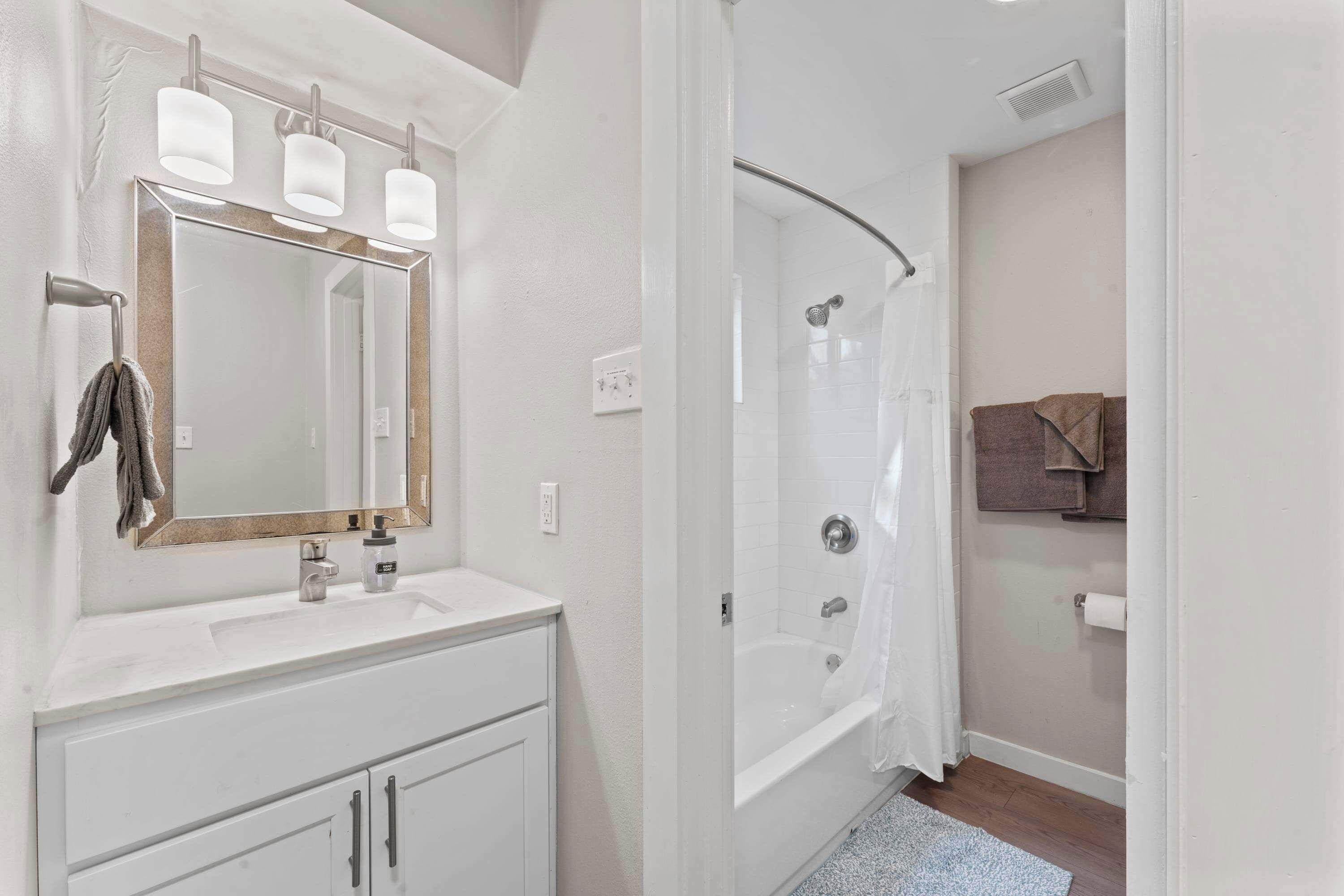 A bathroom with a white vanity, a large mirror, a glass-enclosed shower, and a towel rack.