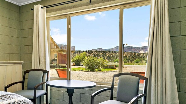 A room with a large window, two chairs, a small table, and a bed with a patterned bedspread. - Mt Carmel Motel close to Zion National Park (Orderville)