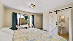 Un dormitorio con una cama grande, un escritorio, una silla, una ventana con cortinas, y un baño con lavabo y espejo.