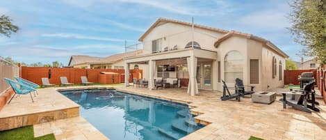 A backyard with a swimming pool, patio furniture, and a barbecue area.