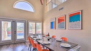 Un coin repas avec une longue table, des chaises orange et une bouteille de vin.