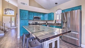 Une cuisine moderne avec des meubles de couleur turquoise, un réfrigérateur en acier inoxydable et un îlot central doté de tabourets.