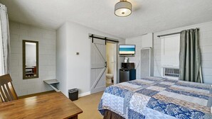 A bedroom with a bed, a television, a window with curtains, a door, and a small table. - Mount Carmel Motel near Zion National Park (Orderville)