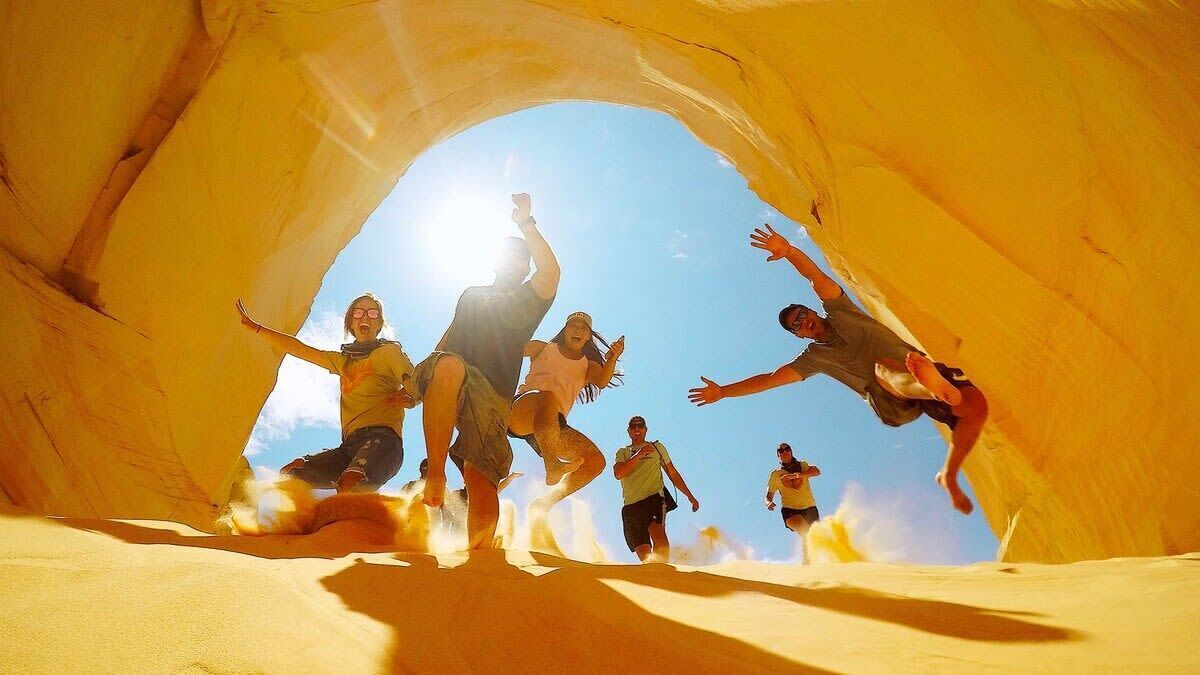 Un grupo de personas dentro de una cueva extensa y natural, con un cielo azul despejado visible a través de una abertura.