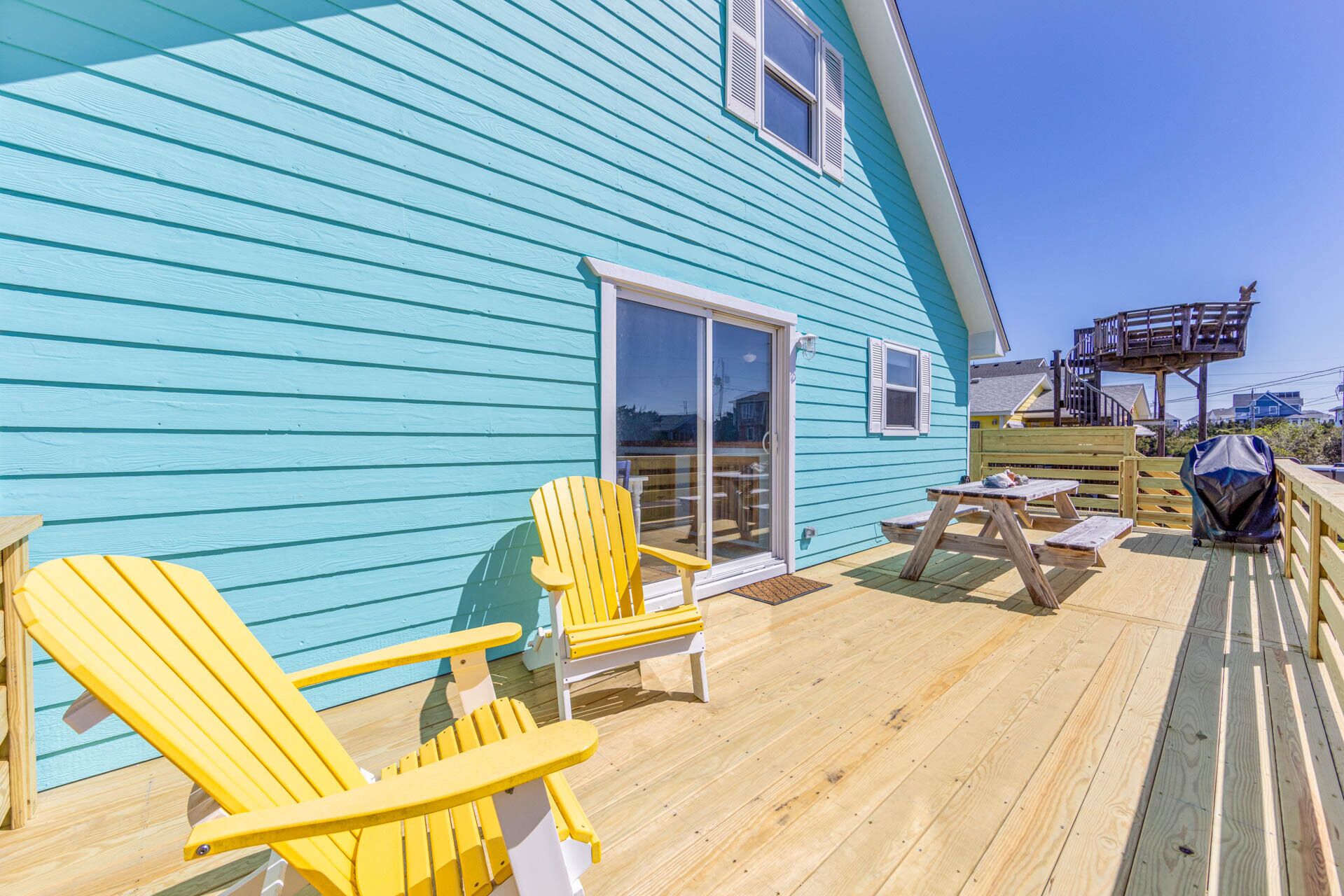 A blue house with a deck, yellow Adirondack chairs, and a picnic table.