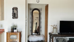 Un salon comprenant un meuble en bois, un téléviseur, un miroir et une porte donnant sur une autre pièce.