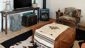 Un salon chaleureux avec un plafond en bois, un meuble TV noir, un poêle à bois bleu, un fauteuil en cuir et un tapis à motifs.