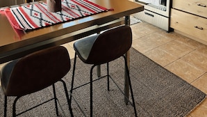 Une cuisine moderne avec des meubles en bois, un réfrigérateur en acier inoxydable, un four à micro-ondes, un four et un évier. On y trouve une table à manger avec deux chaises et un tapis.