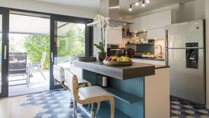 Une cuisine moderne dotée d’un îlot central, d’appareils électroménagers en acier inoxydable et offrant une vue sur l’extérieur.