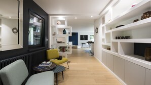 Un salon moderne avec un canapé, un fauteuil jaune, une petite table avec des livres et une bibliothèque.
