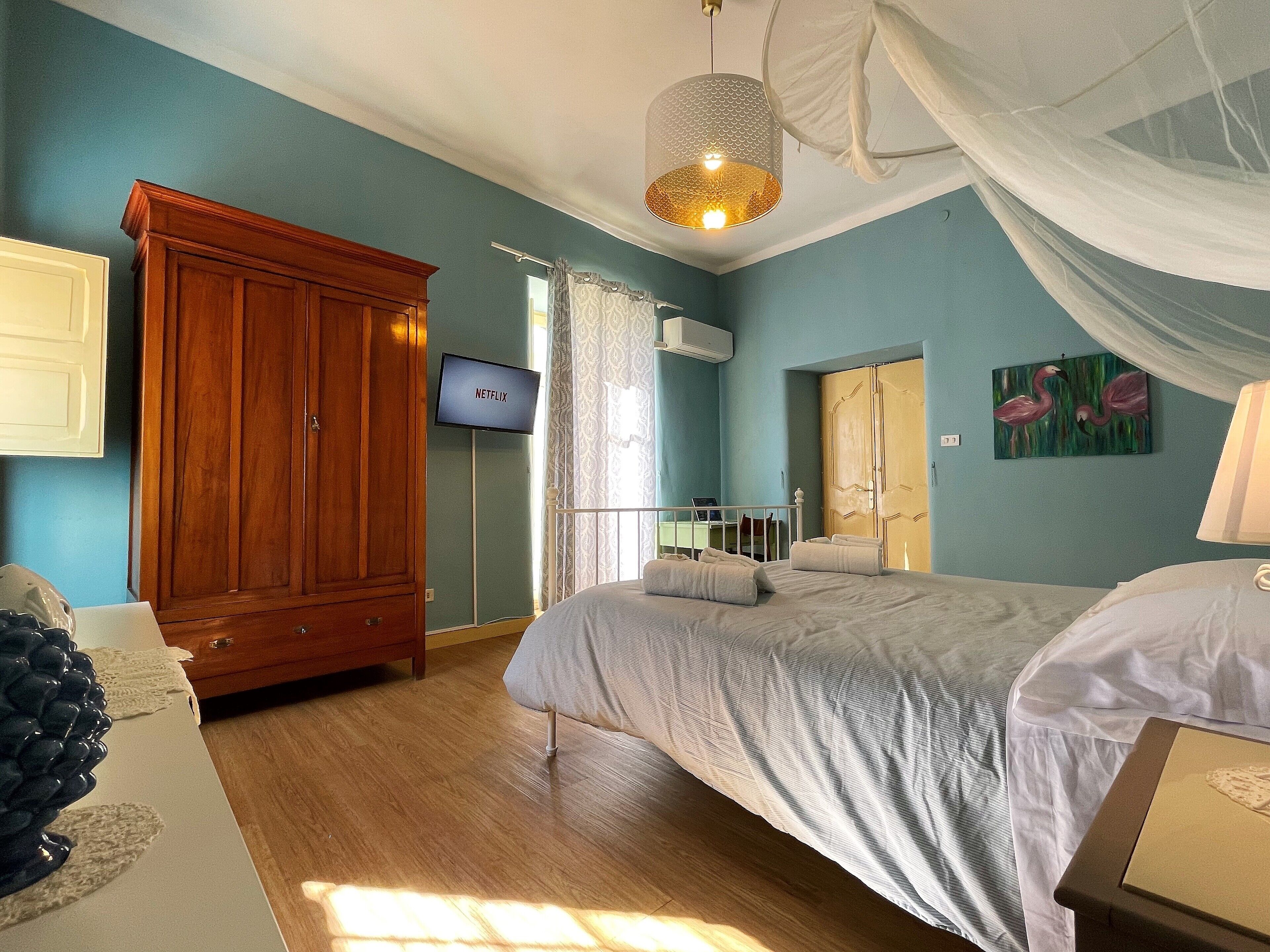Een slaapkamer met een bed, een houten garderobe, een televisie en kunstwerken.