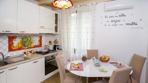 Une cuisine avec des meubles blancs, un pare-feu en carrelage, une cuisinière et un coin repas comprenant une table et des chaises.