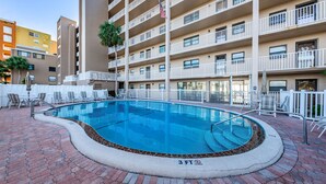 Une piscine avec un panneau indiquant une profondeur minimale de 3 pieds et interdisant la plongée, entourée de chaises longues et d’une terrasse en briques.
