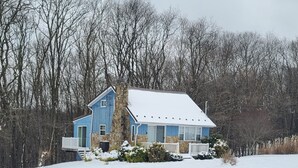 Ein blaues Haus mit einem Steinkamin, umgeben von schneebedecktem Boden und Bäumen.
