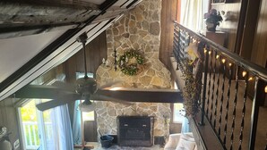 Ein Loft-Wohnbereich mit Kamin aus Stein, einem Balkon mit Geländer und einer gemütlichen Sitzecke mit blauem Sofa.