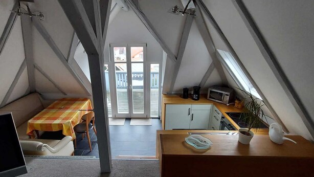 A compact, triangular attic bedroom with a bed, a small table, and a kitchenette.