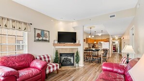 A living room with a fireplace, red leather sofas, a television, and a dining area with wooden furniture. - Mountain View Riverfront Condo W/ Balcony, Fishing, Fireplace, Fitness W/ Sauna (Sevierville)