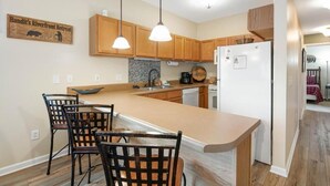 A kitchen with wooden cabinets, a large island with bar stools, pendant lights, and a refrigerator. - Mountain View Riverfront Condo W/ Balcony, Fishing, Fireplace, Fitness W/ Sauna (Sevierville)