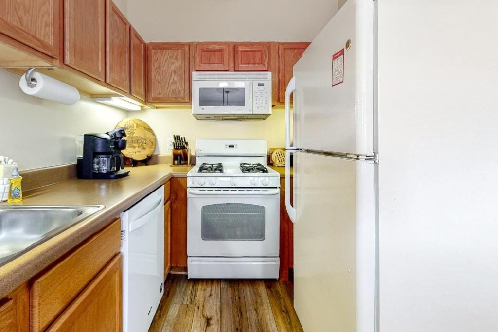 Una cocina compacta con armarios de madera, un microondas blanco, una estufa y un refrigerador.