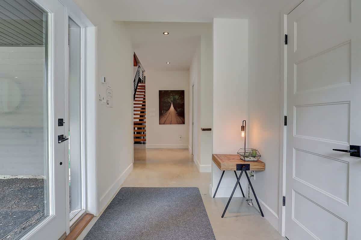 Ein moderner Flur mit einer Holztreppe, einem gerahmten Kunstwerk und einem kleinen Tisch mit einer Lampe.