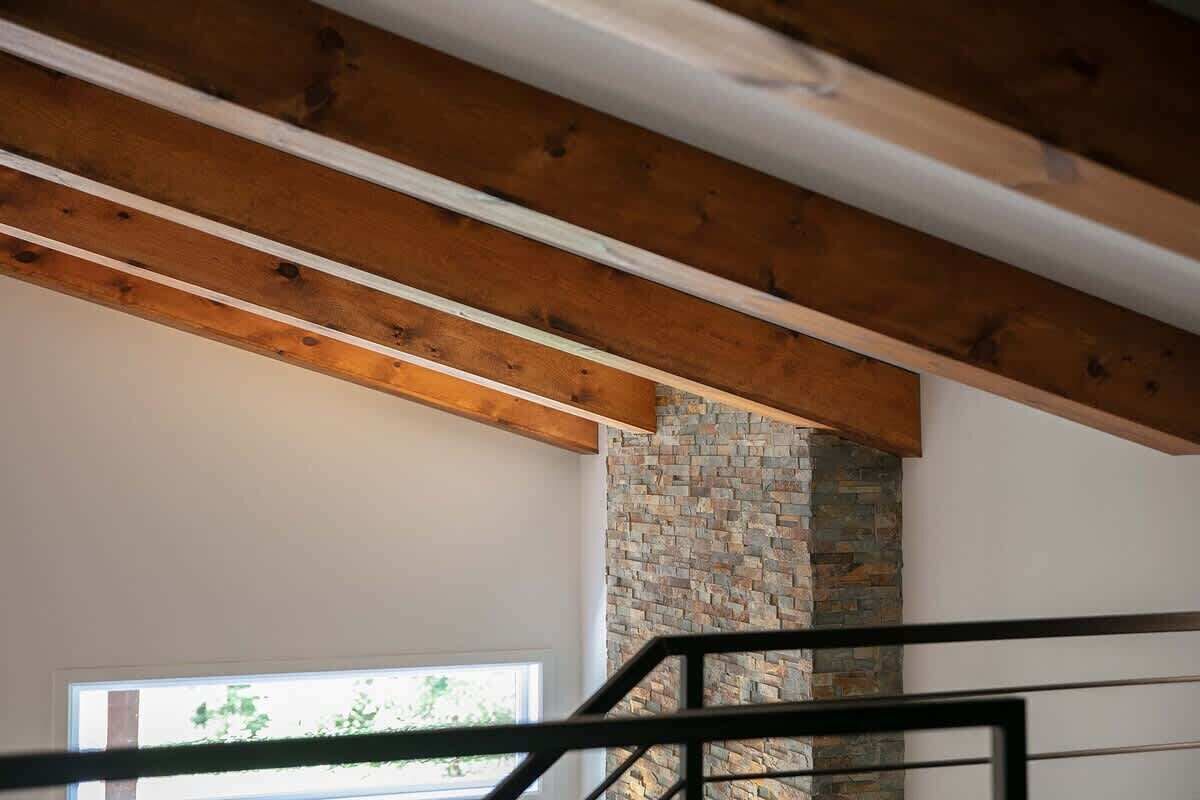 A room with exposed wooden beams, a stone fireplace, and a window.