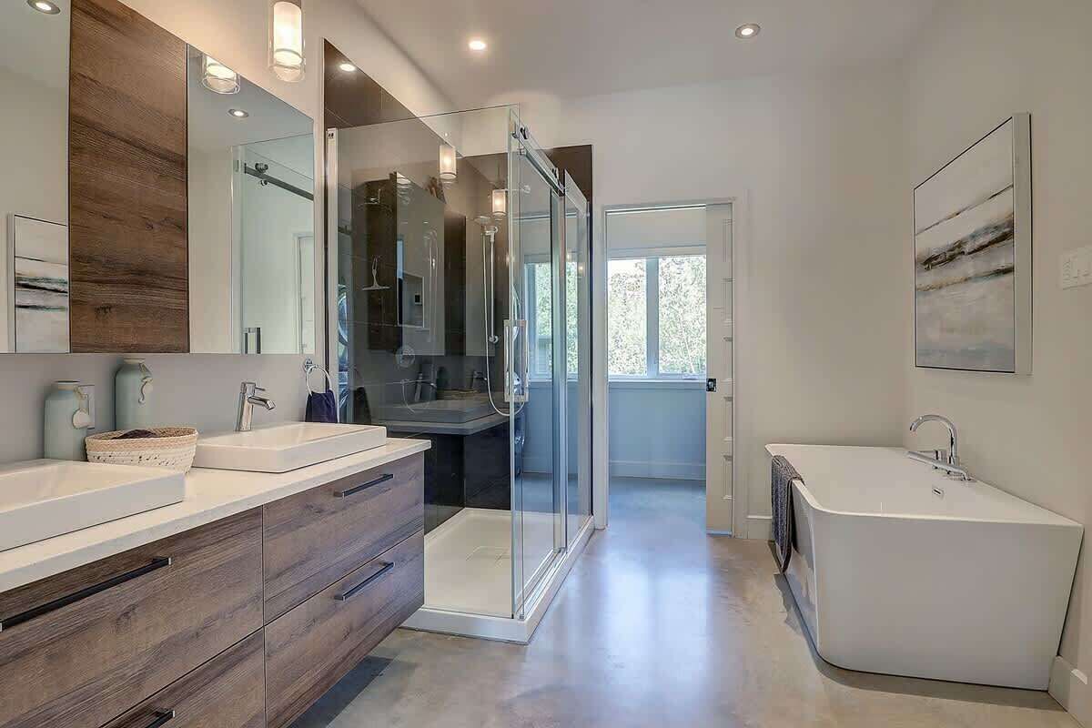 A modern bathroom with a glass shower enclosure, a freestanding bathtub, and a large mirror above the vanity.