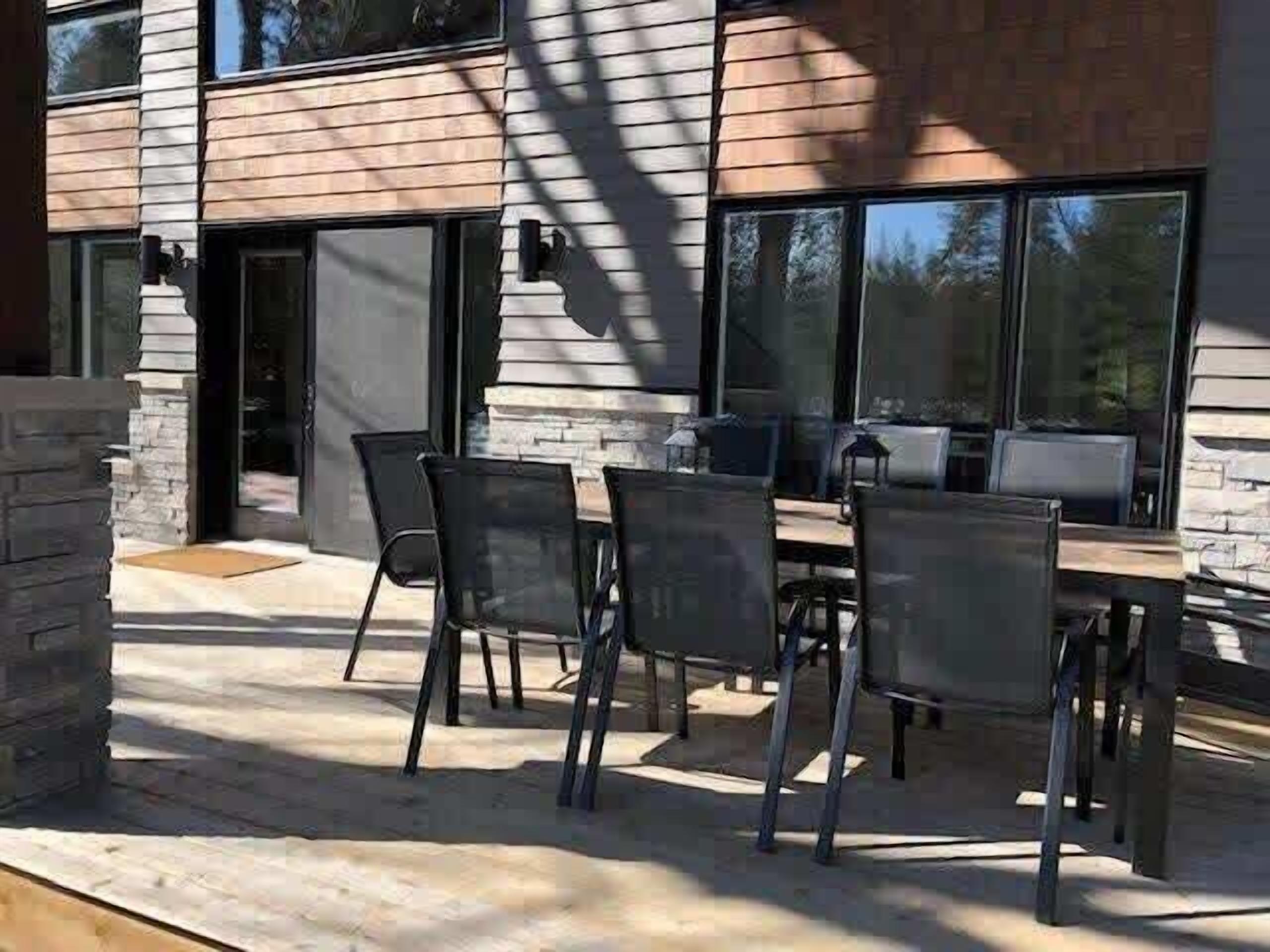 Eine moderne Außenpatio mit Holztisch und -stühlen, Steinverzierungen und großen Fenstern.